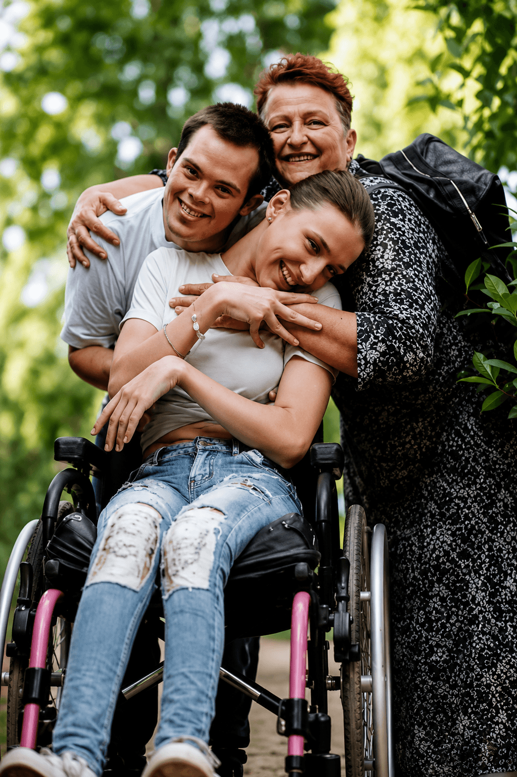 A smiling family embraces a young woman in a wheelchair outdoors, sharing a joyful moment together in a green park.